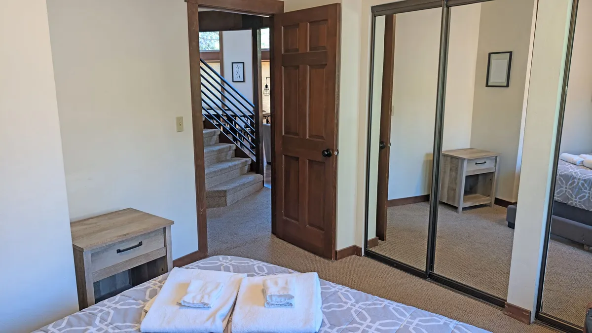 A neatly made bed with towels sits near a mirror wardrobe and a staircase visible in the background. Natural light fills the space, and the overall ambiance is comfortable and cozy, inviting relaxation and easy mornings.