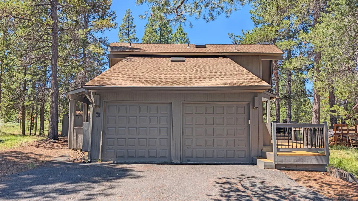 The front exterior of the home with dual garage doors, entrance steps, and a backdrop of towering pine trees. The inviting facade is framed by the natural landscape, hinting at both the spaciousness and the welcoming atmosphere inside.