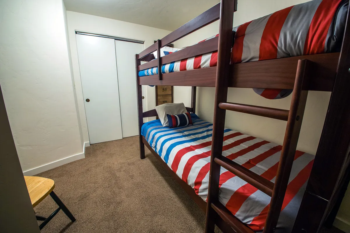 A charming bunk room with a sturdy wooden bunk bed dressed in striped bedding, a small ladder for easy access, and a petite chair in the corner—creating a playful and welcoming atmosphere for kids or guests.