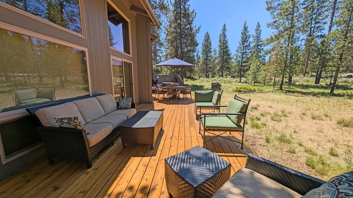A serene outdoor seating area on the deck, with comfortable chairs and an umbrella, surrounded by trees. The setting is tranquil and inviting, ideal for enjoying fresh air, watching pets play nearby, or taking in the forest views after a day of exploration.