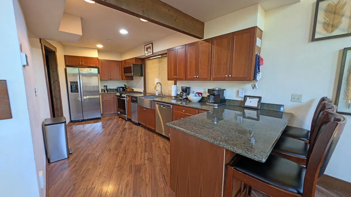 A well-equipped galley kitchen with granite countertops, wooden cabinets, and modern stainless steel appliances. The kitchen flows naturally into the rest of the communal spaces, making it ideal for cooking, entertaining, and group activities.