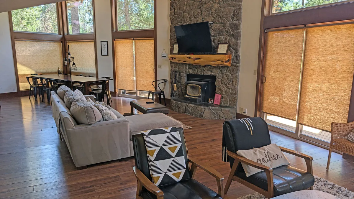 A cozy and welcoming interior scene highlighting a fireplace, large windows, a dining table, and plush seating. The space exudes warmth and togetherness, ideal for family meals, entertaining, or unwinding after a day outdoors.