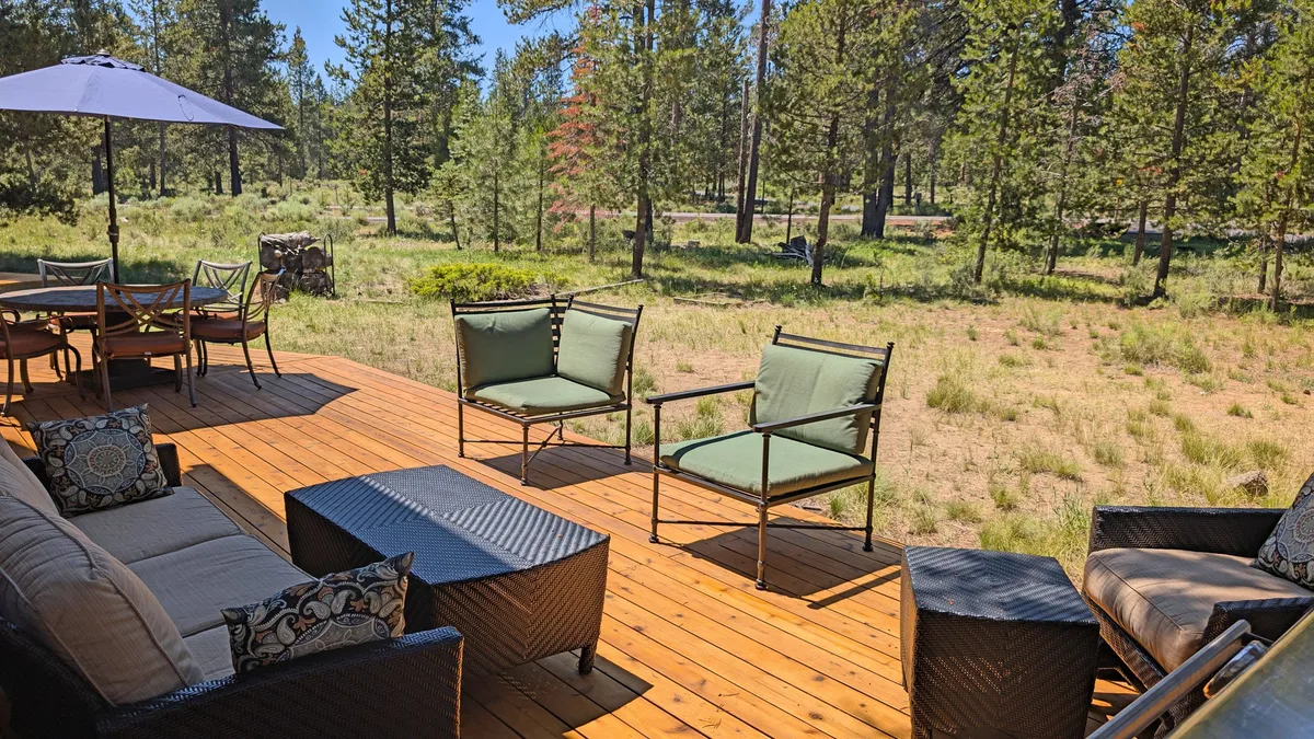 This image focuses on an inviting outdoor seating area atop a wooden deck, with an umbrella for shade and tall trees all around. The space suggests a comfortable spot to relax, socialize, or recharge after a day of adventure—mirroring the experience of recharging an electric vehicle.