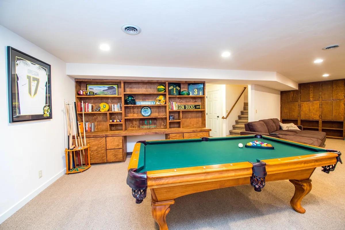 A relaxed lounge area with a pool table, bookshelves, a comfortable sofa, and a framed sports jersey on the wall—perfect for both lively recreation and quiet downtime.