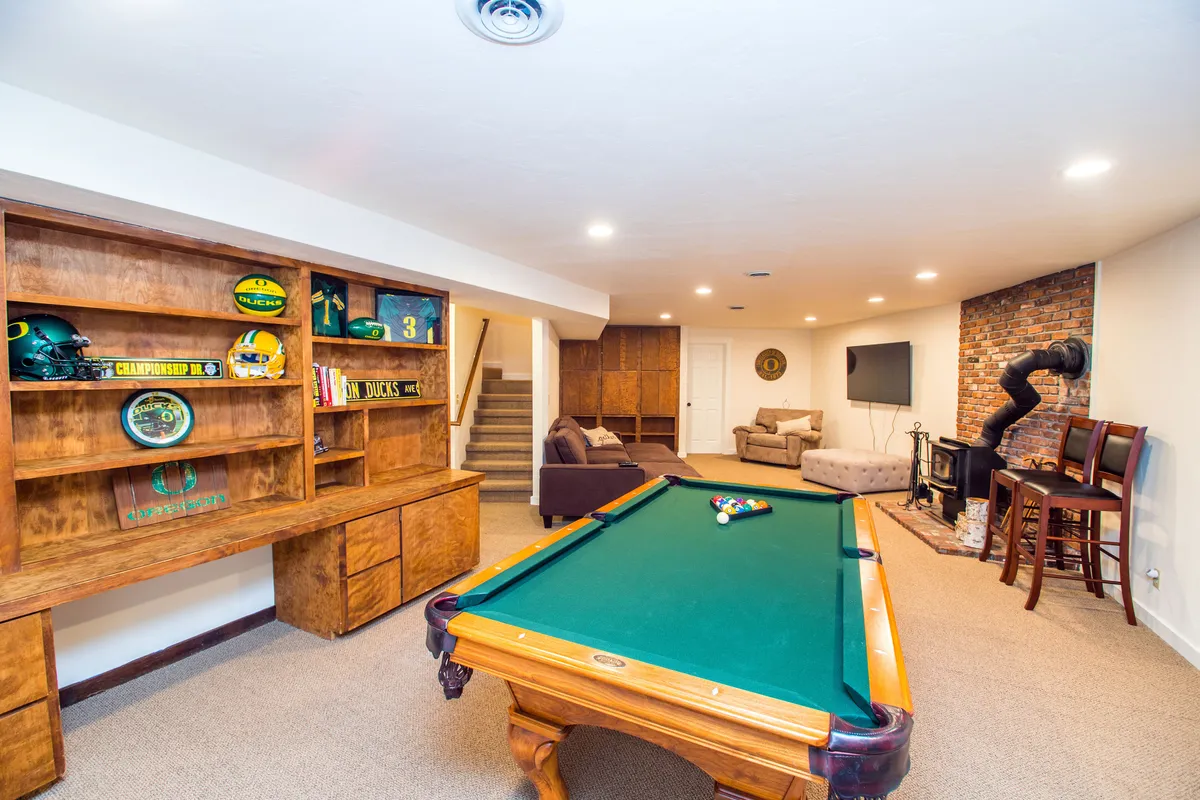 A cozy downstairs entertainment area featuring a pool table, comfortable seating, a bookshelf filled with memorabilia, and a fireplace, creating a social space perfect for friendly games or relaxing with friends after an active day outside.
