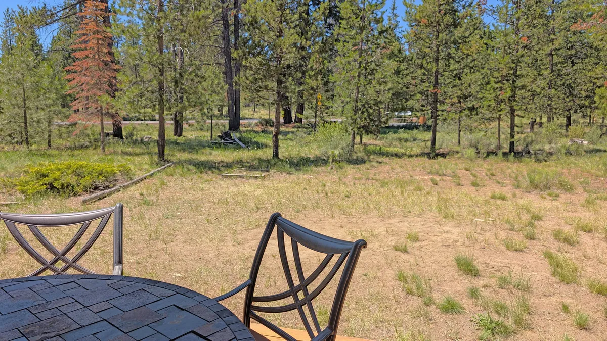 An outdoor dining table set in a grassy clearing, surrounded by tall trees and native vegetation. The area exudes tranquility and is perfect for outdoor meals, wildlife watching, or relaxing in the sun after a morning bike ride or hike.